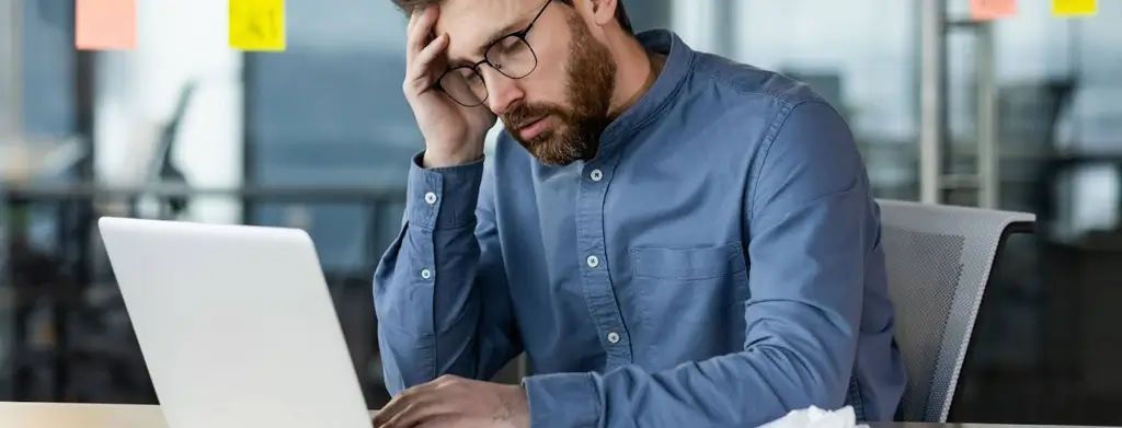 A stressed male working professional sitting at his desk, holding his head in frustration, symbolising workplace tension and a toxic relationship with his employer, illustrating the concept of constructive dismissal.